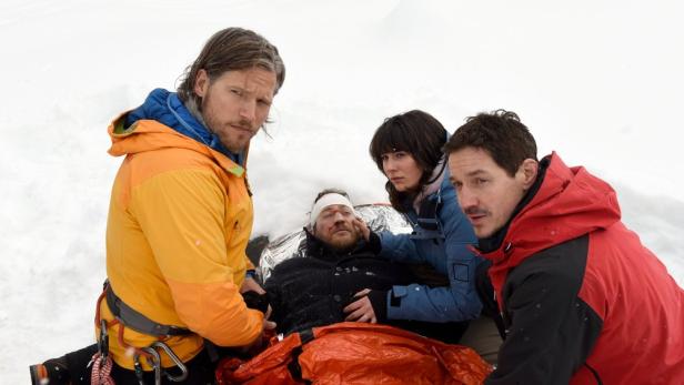Ein verletzter Mann wird von drei Bergrettern im Schnee versorgt.