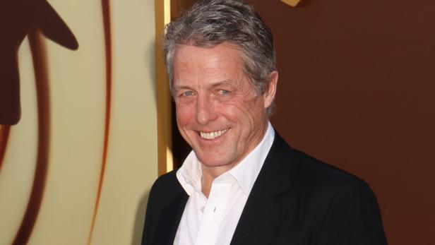 Hugh Grant lächelt in einem schwarzen Anzug.