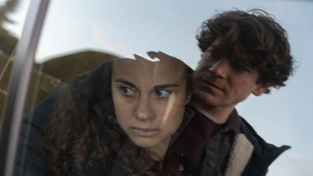 Eine Frau und ein Mann schauen besorgt aus einem Fenster.