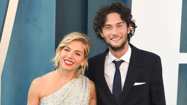 Sienna Miller posiert mit einem Mann in einem dunklen Anzug.