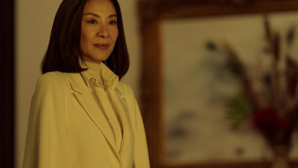 Michelle Yeoh steht in weißen Klamotten in einem weichen Licht da. 