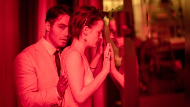 Ein Paar steht in rotem Licht vor einer Glasscheibe.