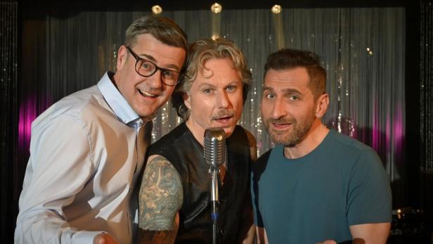 Drei Männer stehen vor einem Mikrofon und scheinen zu singen.