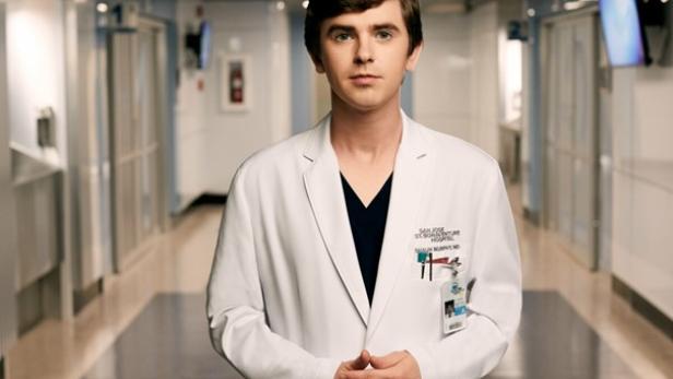 Ein junger Mann steht in einem weißen Kittel in einem Krankenhausflur.