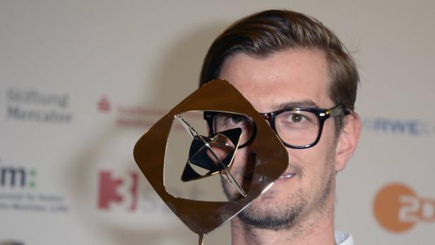 Ein Mann mit Brille hält eine goldene Grimme-Preis-Statue vor sein Gesicht.