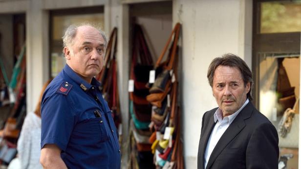 Zwei Männer, einer in Polizeiuniform, stehen vor einem Geschäft mit Taschen.