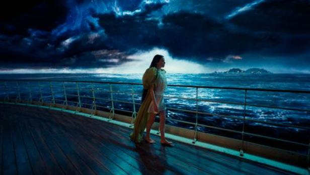 Emma Stone mit langen schwarzen Haaren auf einem Schiff vor einem surrealen Meeres-Hintergrund