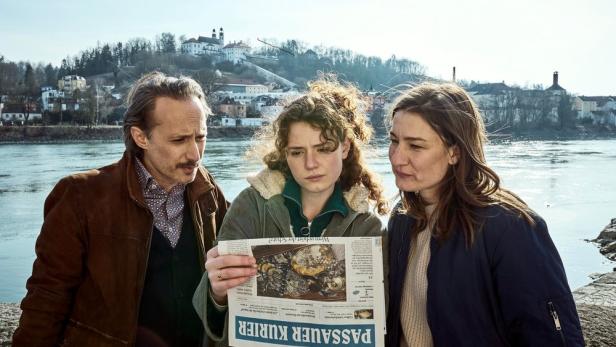 Drei Personen stehen am Ufer und lesen die Zeitung „Passauer Kurier“.