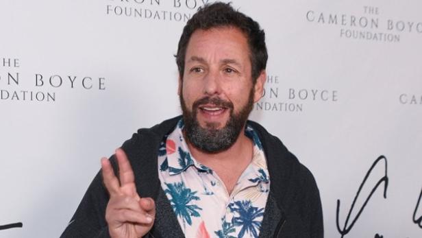 Adam Sandler mit einem Hawaii-Hemd und zeigt das Peace-Zeichen auf dem roten Teppich.
