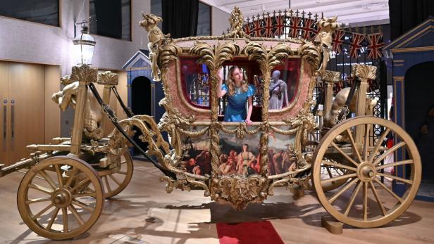 Frau in blauem Kleid steht in einer Kutsche.