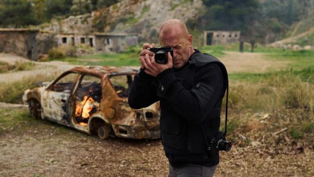 Ein Fotograf macht ein Foto von einem ausgebrannten Auto in einer zerstörten Umgebung.