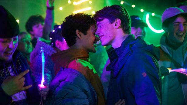 Zwei junge Männer tanzen in einem Club; das Bild ist sehr bunt