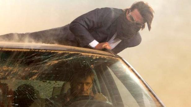 Ein Mann liegt auf der Motorhaube eines Autos, dessen Windschutzscheibe zerbrochen ist.