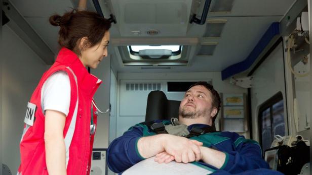 Ein Mann liegt angeschnallt in einem Rettungswagen, während eine Notärztin mit ihm spricht.