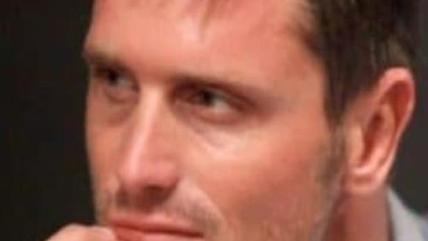 Ein Mann in einem hellblauen Hemd blickt nach links und berührt sein Kinn mit der Hand.