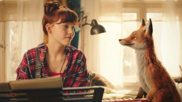 Eine junge Teenagerin mit roten Haaren sitzt im karierten Hemd neben einem Fuchs in ihrem Zimmer.