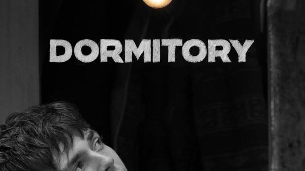 Ein junger Mann blickt in einem dunklen Raum unter einer Glühbirne nach oben, über ihm der Schriftzug „Dormitory“.