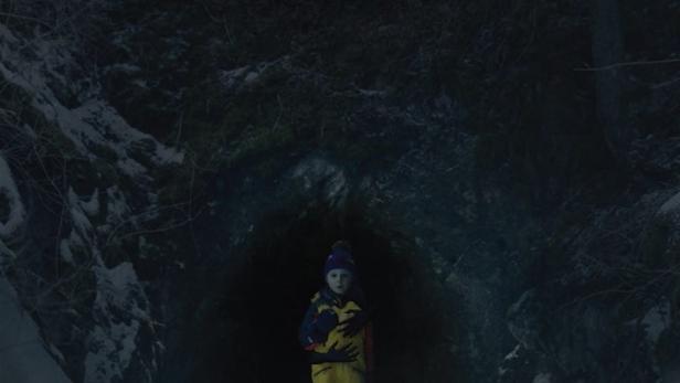 Ein Junge steht vor dem Eingang zu einer dunklen Höhle, Plakat für „From Darkness“.