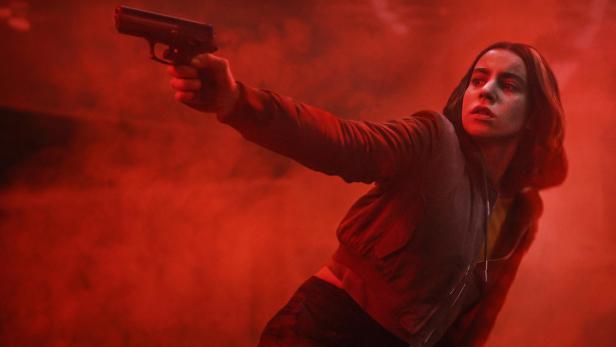 Eine Frau mit gezogener Waffe steht in einem roten Nebel
