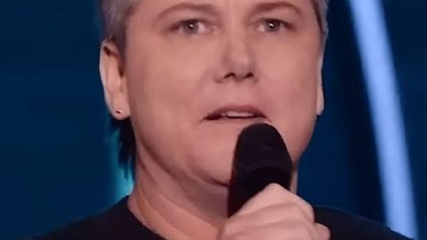 Hannah Gadsby bei einem Auftritt mit Mikrofon, im Hintergrund der Titel „Gender Agenda“.