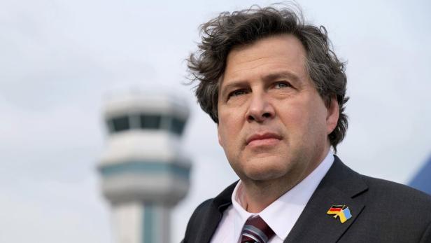 Ein Mann mit Anzug und Anstecknadel mit Deutschland- und Ukraineflagge vor einem Kontrollturm.