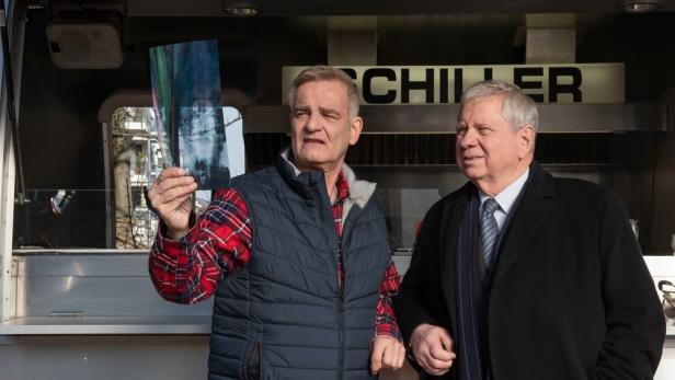 Zwei Männer stehen vor einem Imbisswagen, einer hält ein Röntgenbild hoch.