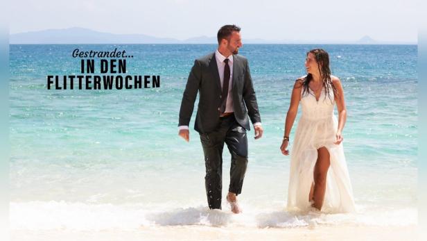 Ein Paar in Hochzeitskleidung watet am Strand im Meer.