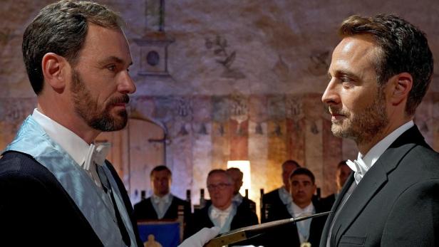 Zwei Männer in Anzügen bei einer feierlichen Zeremonie.