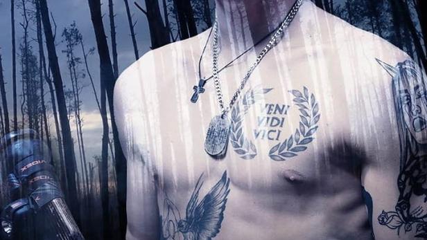 Ein Mann mit Tätowierungen hält ein Gewehr vor einem verschwommenen Waldhintergrund.