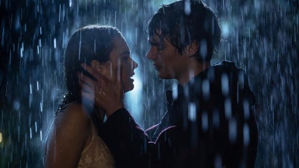 Ein junger Mann und eine junge Frau stehen im Regen. Er hat seine Hände um ihr Gesicht.