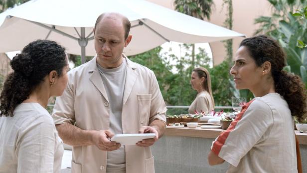 Ein Mann im Arztkittel bespricht etwas mit zwei Frauen im Freien.