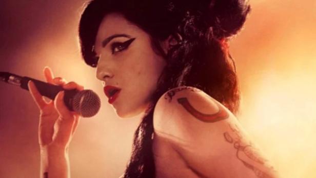Marissa Abela als Amy Winehouse auf eer Bühne. Sie hält ein Mikrofon umgekehrt in der Hand und ist in ihrem typischen Look mit Eye Liner und Hochsteckfrisur zu sehen.