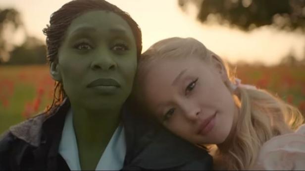 Eine Frau mit einem grünen Gesicht sitzt neben einer Blondine, die ihren Kopf auf ihrer Schulter gelegt hat.