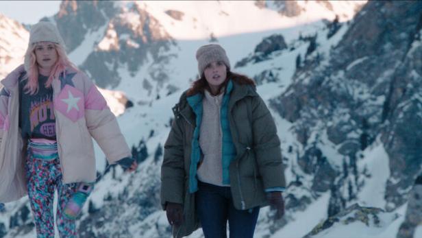 Zwei Frauen stehen in Winterklamotten in den schneebedeckten Bergen