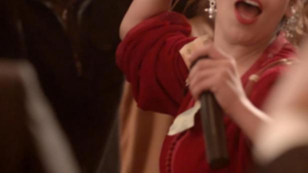 Eine Frau singt in einem roten Kleid mit Mikrofon, umgeben von Menschen.