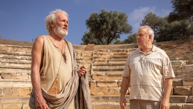 Zwei Männer stehen vor den Stufen eines antiken Theaters.