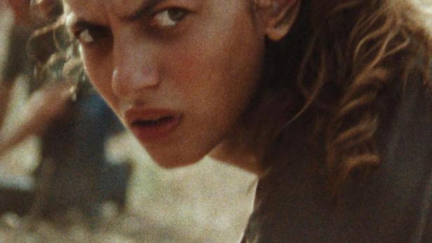 Eine junge Frau blickt mit ernstem Blick über ihre Schulter.