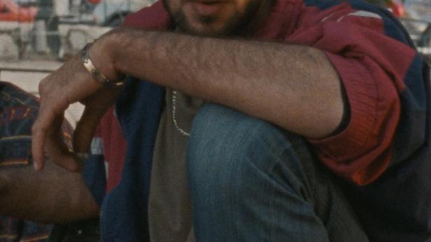 Ein Mann sitzt auf einer Bank im Freien und raucht eine Zigarette.