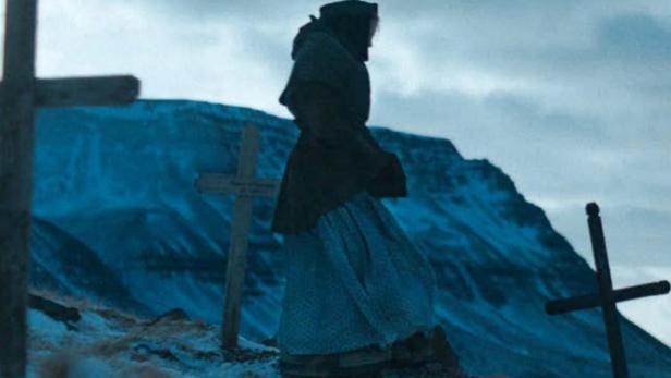 Eine Frau steht auf einem schneebedeckten Hügel mit Kreuzen vor einem Berg.