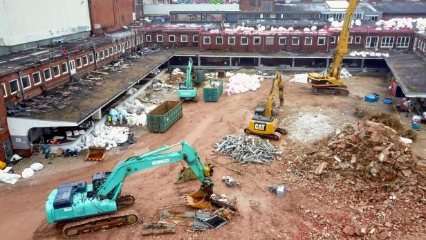 Mehrere Bagger sind auf einer Baustelle im Einsatz, um ein Gebäude abzureißen.