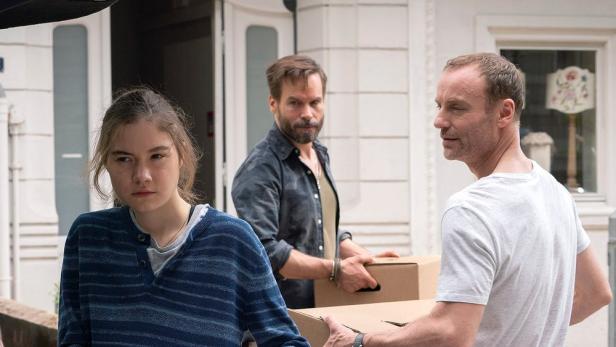 Eine junge Frau und zwei Männer tragen Umzugskartons vor einem Haus.