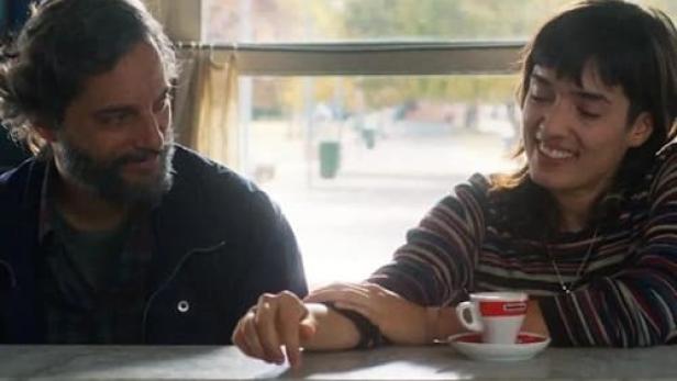 Ein Mann und eine Frau sitzen an einem Tisch mit einer Tasse Kaffee, Szene aus „El Aroma del Pasto Recién Cortado“.