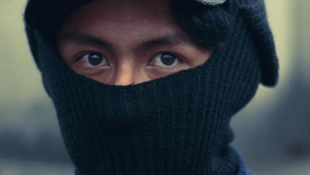 Ein Mann mit Sturmhaube und Mütze blickt in die Kamera, Filmposter „Perros“.