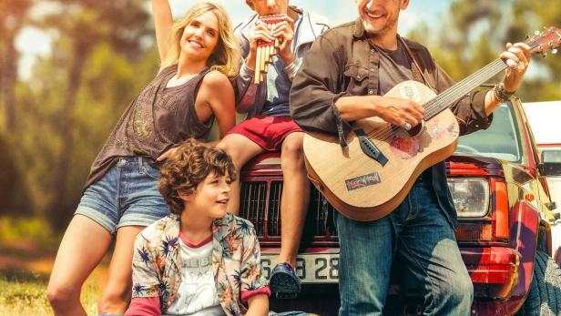 Das Filmplakat für „La Famille Hennedricks“ zeigt eine Familie mit Gitarre und Panflöte vor einem roten Auto, dazu ein Huhn.
