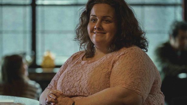 Eine lächelnde Frau in einem rosa Kleid sitzt an einem Tisch.