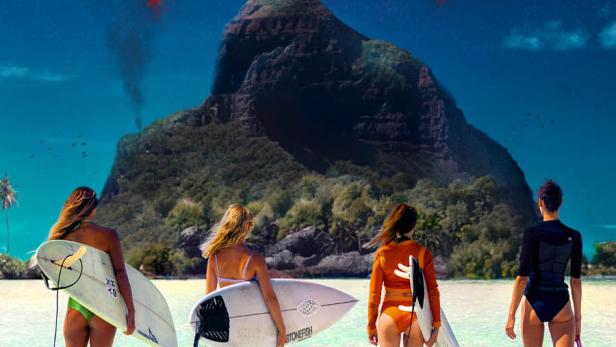 Vier Surferinnen stehen mit ihren Surfbrettern im türkisfarbenen Wasser vor einer tropischen Insel.