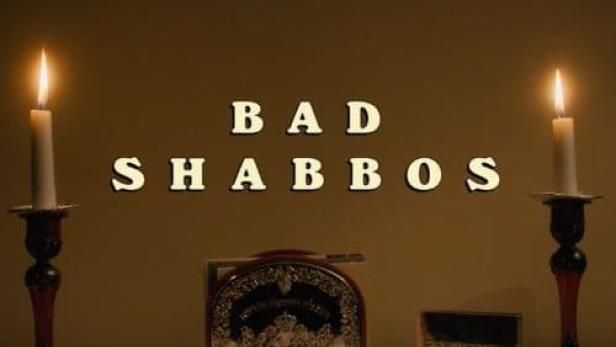 Zwei Kerzenleuchter flankieren den Schriftzug „Bad Shabbos“ auf einem Tisch.