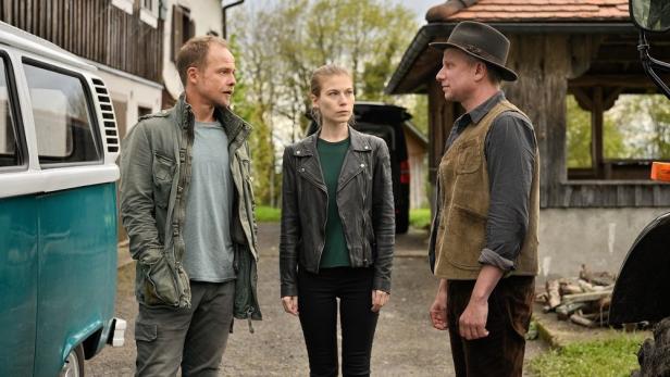 Drei Personen stehen vor einem Haus und einem VW-Bus, möglicherweise eine Szene aus „Toten See“.