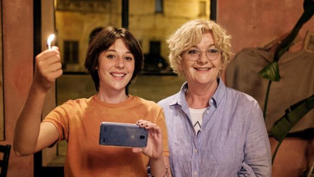 Zwei Frauen, eine mit einem Feuerzeug und die andere lächelnd, posieren für ein Foto.