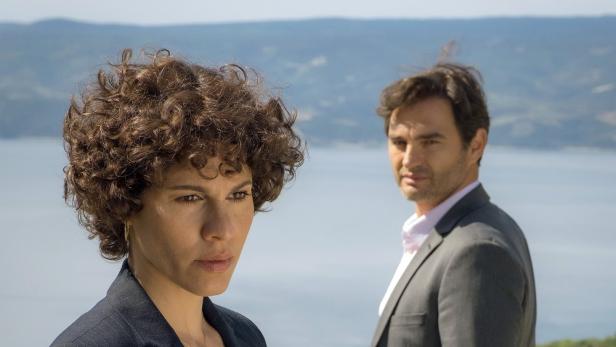 Eine Frau und ein Mann vor einer Küstenlandschaft im „Kroatien-Krimi: Tod im roten Kleid“.